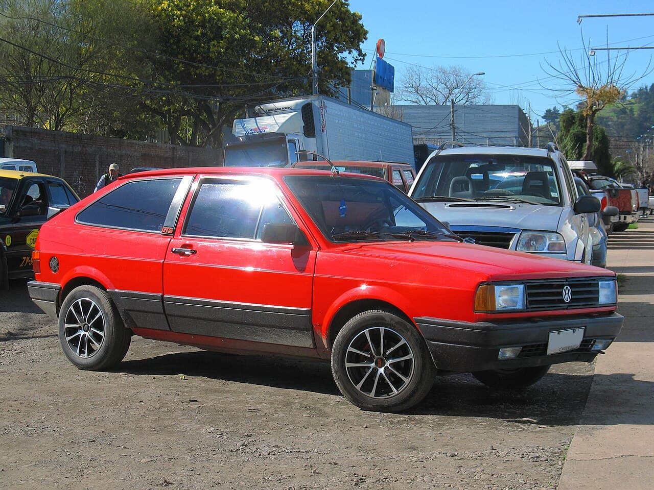 Volkswagen Gol GTS rojo de tres puertas, visto desde adelante y de costado, con llantas de aleación y la insignia GTS en la columna trasera.